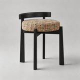 A modern upholstered dining chair with a black wooden frame and a round tufted seat cushion in a textured multicolor tweed fabric, photographed on a neutral light gray background.