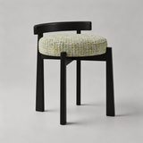 A wooden dining chair with a curved backrest, four tapered legs, and a round tufted seat cushion upholstered in a multicolor tweed fabric, shown against a neutral light gray background.
