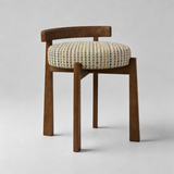 A mid-century modern wooden dining chair with a curved backrest, solid medium-brown legs, and a round upholstered seat cushion featuring a multicolor geometric pattern on a light beige background.