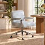A modern office chair with a light blue and white gingham patterned fabric and chrome metal armrests and base, positioned in a bright, sunlit home office next to a wooden desk.