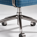 Close-up of an office chair base with a polished chrome five-star metal frame and black casters, showing part of a blue plaid upholstered seat.