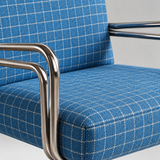 Close-up of a blue upholstered chair with a white windowpane plaid pattern and polished chrome tubular metal arms.