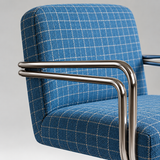 Close-up of a blue plaid upholstered chair with a polished chrome tubular metal armrest.