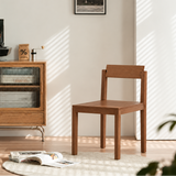 Brown wood dining chair on a cream rug beside a glass-front cabinet in a sunlit room.
