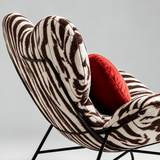Rear close-up of the zebra-print lounge chair showing its heart-shaped backrest, stitched edges and black metal frame.
