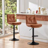 Two cognac tufted bar stools with black pedestal bases beside a sunlit kitchen island.