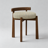 Brown wooden vanity stool with a low curved backrest, round cream textured seat cushion and four tapered legs.
