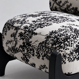 Close-up of the botanical accent chair seat cushion showing ivory and black fabric, piping and a black front leg.

