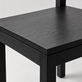 Close-up of the black dining chair's flat wood-grain seat, straight edges and square frame joints.
