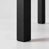 Close-up of the black dining chair's square leg, showing vertical wood grain and softly rounded bottom edges.
