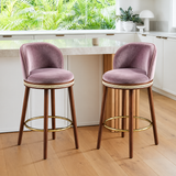 Two mauve Alma bar stools with dark wood legs and gold-tone footrests beside a white kitchen island.
