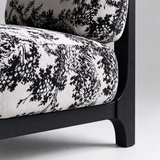 Close-up of the botanical accent chair showing patterned cushions, the black side rail and rear leg.

