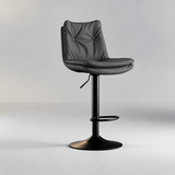 Slate grey bar stool with a two-button tufted backrest, padded seat, black pedestal base and oval footrest.