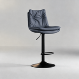 Dark slate blue bar stool with a button-tufted backrest, padded seat, black pedestal base and oval footrest.