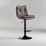 Slate grey bar stool with a two-button tufted backrest, padded seat, black pedestal base and oval footrest.

