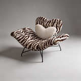 Brown and cream zebra-print lounge chair with a heart-shaped backrest, cream heart cushion and black metal legs.
