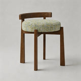 A modern wooden stool with a curved backrest and a round woven seat cushion in a textured light green and beige tweed fabric, shown against a neutral light gray background.