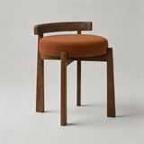 A modern wooden dining chair with a curved backrest, dark brown wood legs, and a round rust-orange upholstered seat cushion, photographed on a neutral light gray background.