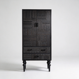 Tall black cabinet with geometric carved double doors, three lower drawers and turned legs against a light background.