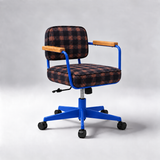 A modern office chair with a blue metal frame, black and orange plaid fabric upholstery, and light wood armrests, shown on a light gray studio background.