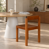 Rear three-quarter view of a brown wood dining chair beside a round table with a white pedestal base.
