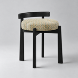 Black wooden vanity stool with a low curved backrest, round cream textured seat cushion and four tapered legs.

