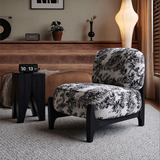 Ivory and black botanical accent chair beside a black side table and floor lamp in a living room.

