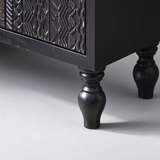 Close-up of the black cabinet's turned legs, smooth side panel and carved lower drawer detail.