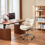 Cream padded office chair with a chrome castor base beside a wooden computer desk and bookshelf in a sunlit home office.