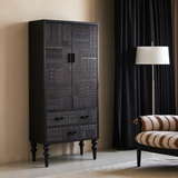 Angled view of a tall black carved cabinet with turned legs beside a striped chair and floor lamp.