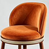 Close-up of the orange Alma bar stool's curved padded backrest, piped edges and round upholstered seat.
