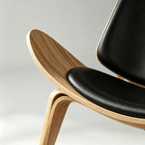 Close-up of the lounge chair's upswept natural wood seat shell, black cushion and curved front leg.
