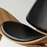 Close-up of the lounge chair's black contoured seat cushion and padded backrest within a natural wood shell.
