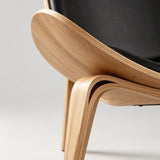 Close-up of the lounge chair's curved natural wood shell and bent leg joint, showing wood grain and layered edges.
