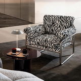 A modern armchair with a bold black and white zebra-patterned upholstery and a chrome metal frame, styled in a contemporary living room setting next to a dark round coffee table.