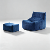 A modern blue upholstered lounge chair with a matching ottoman, both featuring vertical channel tufting, photographed on a clean light gray studio background.