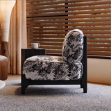 Side view of an ivory and black botanical accent chair with a black frame beside wooden window blinds.

